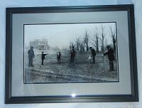 Framed black and white photo showing early golfers in period clothing, set outdoors with leafless trees and buildings in background.