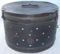 Front angled view of antique metal surgical sterilizer lid closed, showing handle and wear on greenish metal surface.