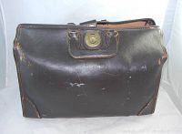Front view of vintage brown leather flight case duffel bag showing wear, scuffs, stress marks, and brass turn-lock closure.