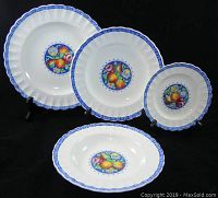 Four pieces of dinnerware displayed showing the dinner plate, salad plate, bread and butter plate, and soup bowl with their blue border and fruit center design.