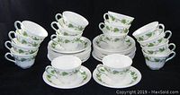 Full view of the 15 sets of flat cups and saucers arranged neatly, showing the green ivy decoration and scalloped edges.