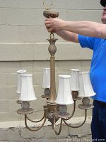 Chandelier held up showing metal arms and white lampshades, pineapple design visible on holders.