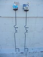 Full view of two metal grass cup holders with decorative figures.