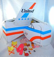 Photo of Barbie Friendship Case shaped like airplane tail with United logo, foldable chairs and various small accessories on floor inside case.
