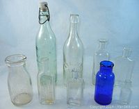 Group of 9 antique bottles of varying sizes and colors against a neutral background revealing shape and transparency