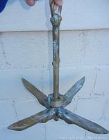 The brass collapsible boat anchor shown unfolded with four flukes extended, held upright to display structure and wear.