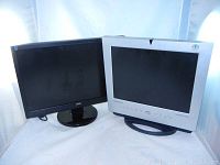 Two monitors side by side on white background, one black AOC with a VGA cable and one silver LCD monitor without cables.
