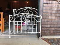 White iron footboard with decorative scroll and floral design, standing upright in garage