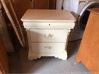 Front view of the painted nightstand showing two drawers, decorative handles, and overall condition.