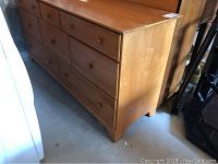 Full side view of the 8-drawer wood dresser showing the natural wood finish and bracket feet.