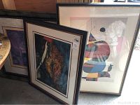 Three large framed art pieces leaning together. Visible are dark frames, print with bride and groom, and colorful abstract art.