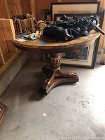 Full view of the round table with solid wood claw foot base and marble top, placed in a garage setting with some items on top.