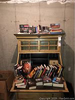 Books arranged on and inside a wooden desk hutch, featuring multiple titles and stacked in piles.