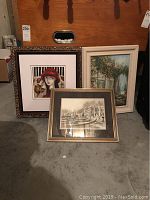 Three framed art pieces leaning against wall on concrete floor showing all three in one photo