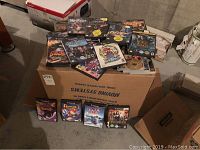Photo of Nintendo GameCube game cases stacked on a cardboard box and on the floor, showing various titles including Harry Potter, Lord of the Rings, Godzilla, Star Fox, 007 Nightfire, and others.