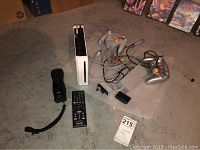 Nintendo Wii console, two GameCube controllers, black Wii remote, Sony TV remote, power and AV cables arranged on floor.