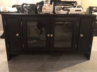 Front view of black TV console with two doors, one solid and one glass panel, with round silver knobs.