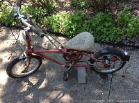 Left side profile showing red Dahon folding bike with fabric-covered saddle on a sunny outdoor surface.