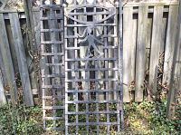 Full view of iron door gate leaning against wooden fence
