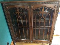 Front view of the wooden cabinet showing glass doors with decorative wood overlay and keys included. Two doors, one with broken glass panel.