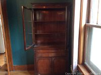 Front view of wooden china cabinet with one glass door open, showing shelves inside and pullout drawers below.