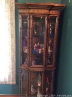 Full front view of wooden curio cabinet filled with decorative figurines and collectibles inside. Shows overall design, bamboo-style wood framing, and glass panels.