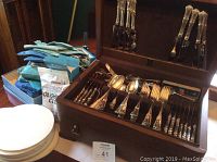 Hinged wooden chest open showing Birks sterling silver flatware arranged in slots and polishing cloths at left
