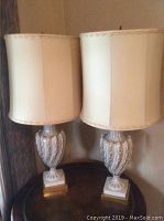 Two matching ceramic based table lamps with beige fabric shades shown on a round table.