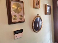 Wall showing round mirror with ornate gold frame and framed barometer with two smaller dials beneath.