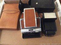 Polaroid SX-70 Land Camera with brown leather accents, full frontal view, alongside a Canon Speedlite 1994 flash.