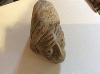 Front view of the carved stone sculpture showing detailed human face features and hair texture.