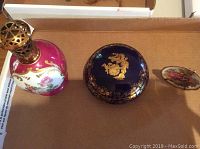 Lamp Berger Paris ceramic perfume lamp with pink and white floral design and brass lattice top, alongside two decorative Limoges plates.