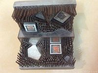 Front view of two stacked metal blocks covered in steel nails with embedded geometric shapes