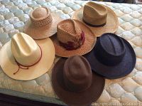 Six men's hats arranged on a mattress showing varied styles and colors
