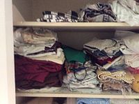Shelf with stacks of assorted folded linens including towels, sheets, and blankets in various colors and patterns.