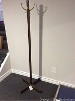 Full view of the wooden coat rack with brass hooks, showing base and height against a wall.