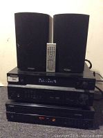 Overall view: two Paradigm speakers flanking a silver remote on top of stacked electronics (Pioneer receiver, Pioneer DVD player, Yamaha CD changer).