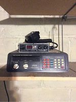 Side-on frontal clear photo of the Realistic 20 channel AM/FM scanner radio unit with volume and squelch knobs, multi-colored keypad and CB microphone with cord on top.
