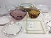 Multiple assorted clear glass bowls, rectangular and round baking dishes, some tinted in purple and amber colors, with clear lids and white ceramic dishes with blue cornflower design.