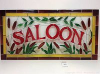 Full view of stained glass saloon sign with red letters and botanical motifs surrounded by a yellow and amber border.