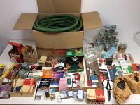 Wide view showing entire lot of garden hose, jars of hardware, hand tools, nails, and other small items spread out on table.