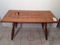 Front view of the solid wood cribbage table with cribbage holes and pegs on the surface.