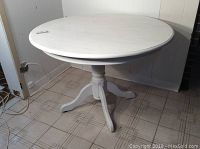 Full view of the round white kitchen table showing the tabletop and pedestal base on tiled floor