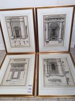 Four framed architectural prints leaning against a wall, showing the front view of each print and partial frame damage