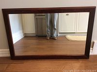 Front-facing full view of large wood framed mirror resting against wall on hardwood floor, showing overall condition and size.