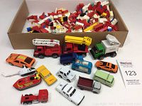 Photo of toy vehicles and Lego pieces in box showing variety of vehicles in assorted colors and mixed Lego bricks.