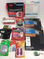 Photo of 3M brand new household items laid out including window insulator kits, sandpaper sheets, weatherstripping, adhesive hooks, LED eyewear, and strap hooks.