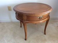Side view of round wooden table on carpet. Shows round top and four curved legs.