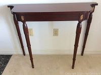 Front view of mahogany coloured console table showing four fluted legs and surface wear.