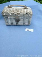 Front view of the rectangular wicker purse, showing the leather handle and metal clasp closure on the front.